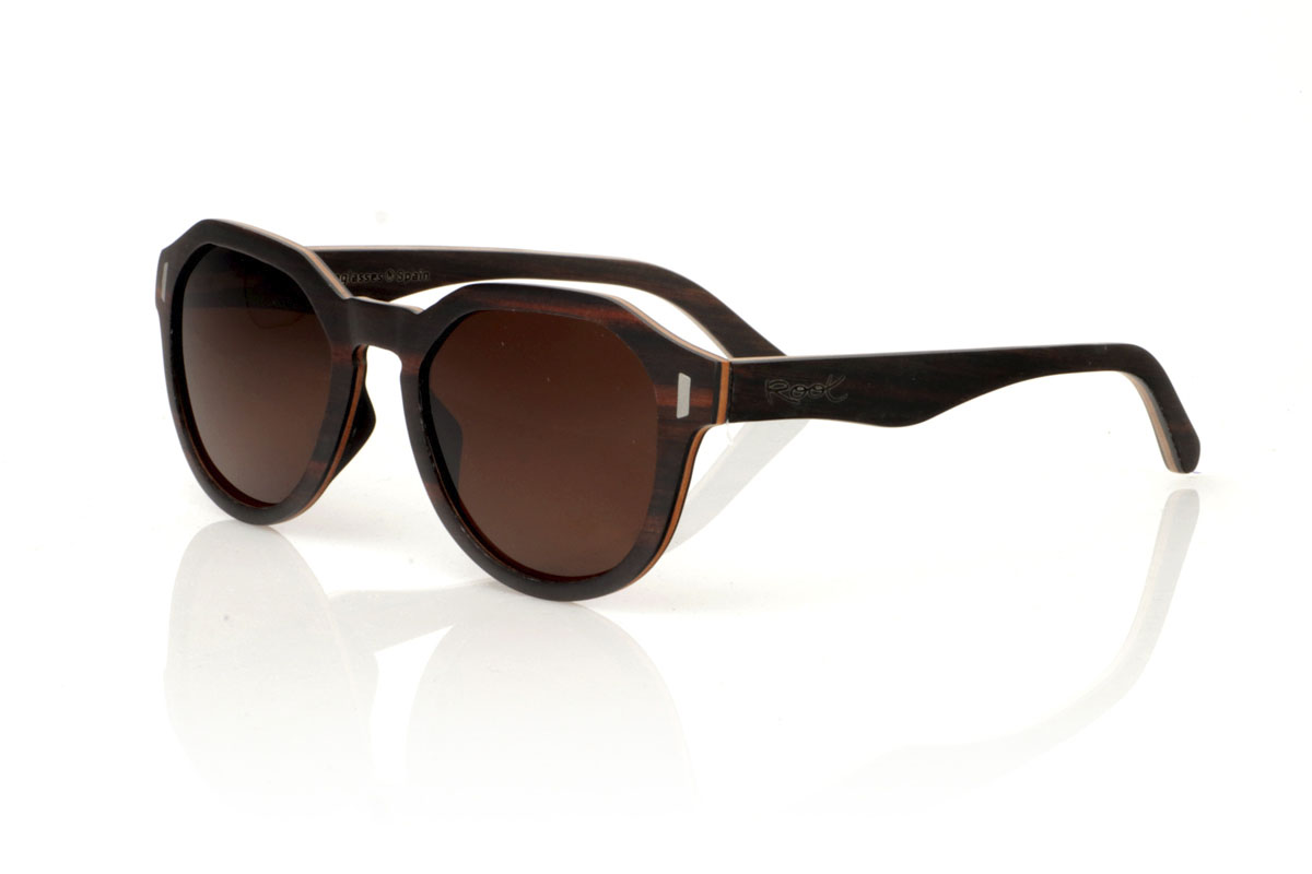 Wood eyewear of Ebony IZARO. IZARO wooden sunglasses are an expression of style and craftsmanship, made entirely of laminated ebony wood both outside and inside, with an intermediate layer of maple wood that provides a clear and striking contrast. The distinctive black and brown grain of the ebony is perfectly complemented by the distinctive hexagonal shape on the brow, while the silver metallic inlays on the sides add a touch of elegance and sophistication. With measurements of 145x50 and a caliber of 51, the IZARO are presented as a perfect option for those looking to stand out with a unique accessory that combines the natural beauty of wood with an innovative design. for Wholesale & Retail | Root Sunglasses® 